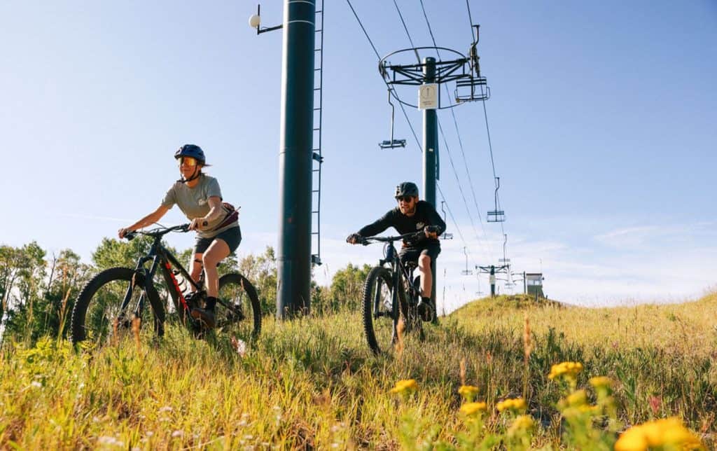 Two people biking down a scenic mountain under a chair lift